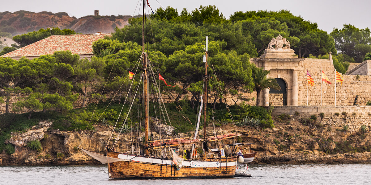 Barco y antiguas ruinas en viaje en coche de alquiler en Menorca